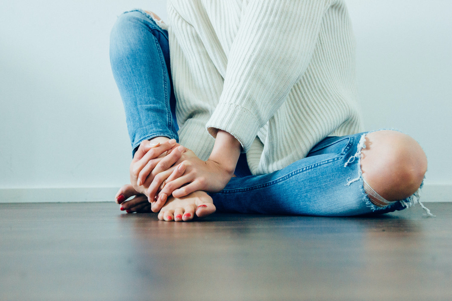 women sitting on floor in white sweater and jeans, barefoot