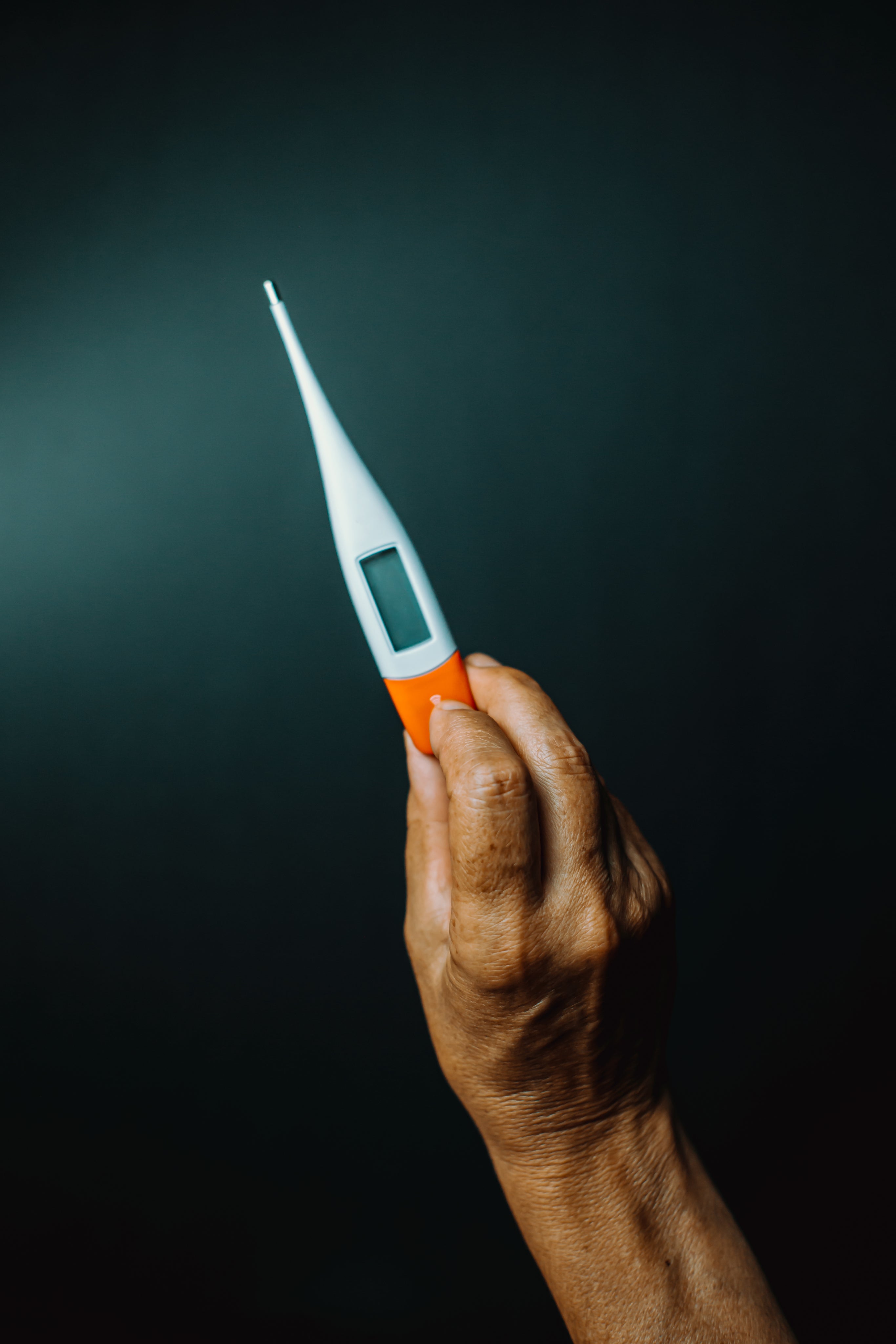 A-HAND-HOLDS-UP-A-THERMOMETER-AGAINST-green-BACKGROUND