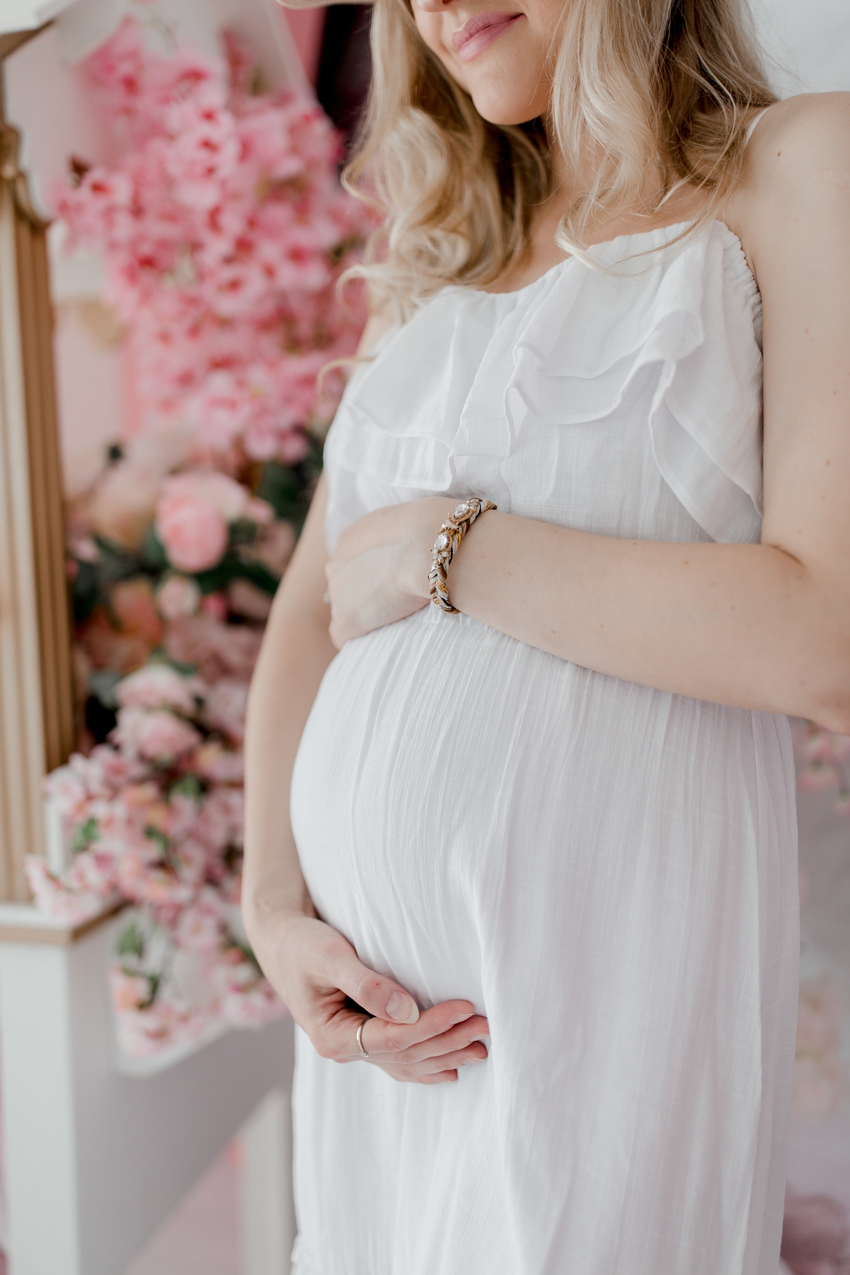 blonde woman standing by pink flowers holding pregnant belly